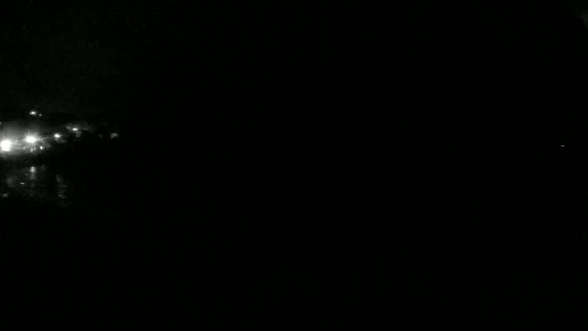 A nighttime image shows a blurry, bright cluster of lights in the distance on the left side, against a completely dark background.