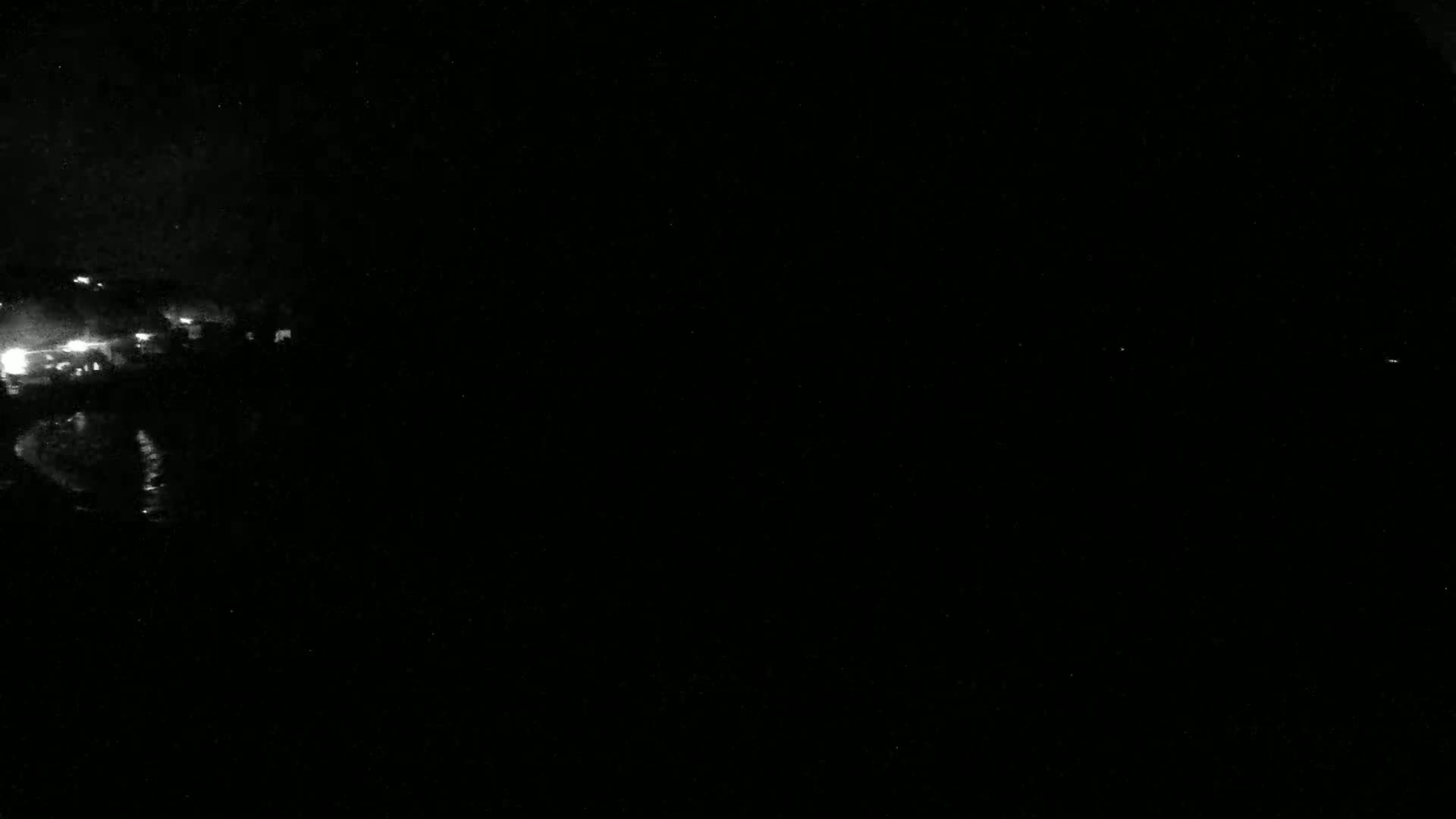 A nighttime, low-light image shows a small cluster of lights in the distance to the left, against a mostly dark background.