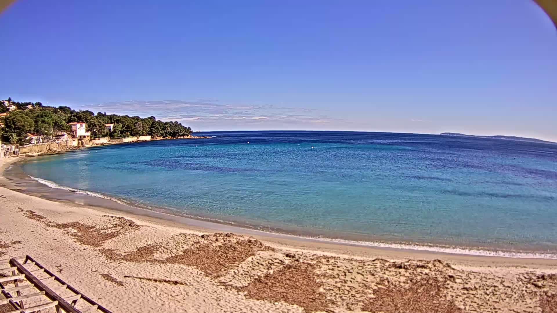 A sandy beach curves around a calm, turquoise bay under a clear blue sky.