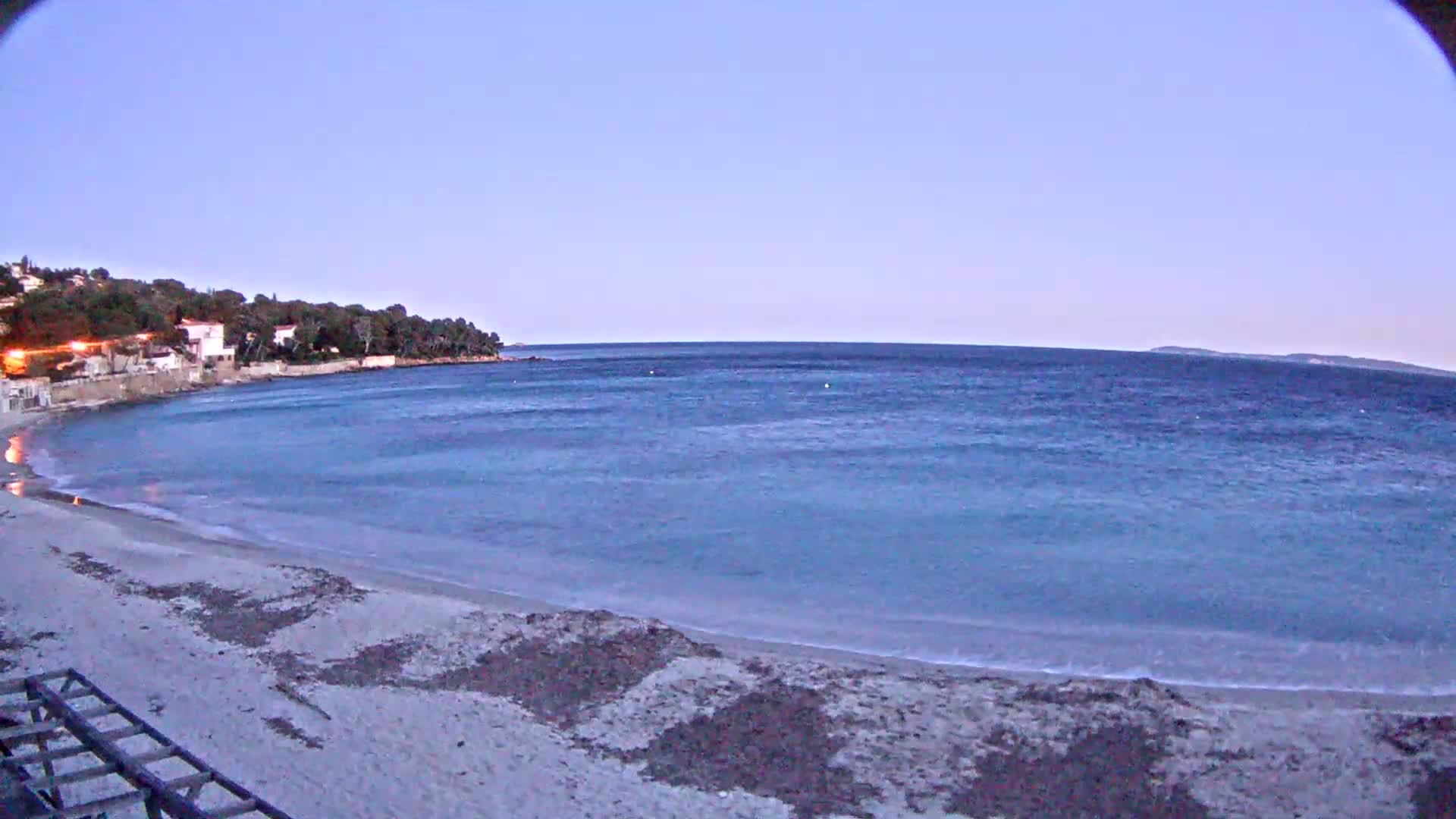 A sandy beach curves gently into a calm, blue sea under a twilight sky.