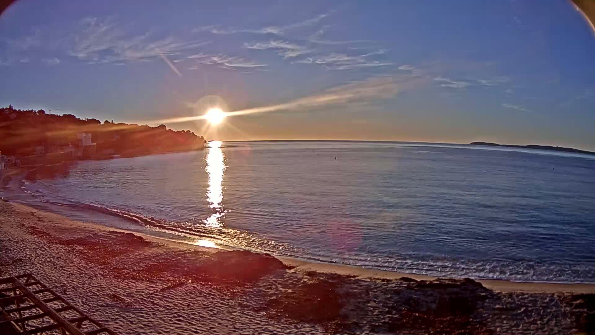 A sandy beach with gentle waves laps the shore at sunset under a mostly clear sky.