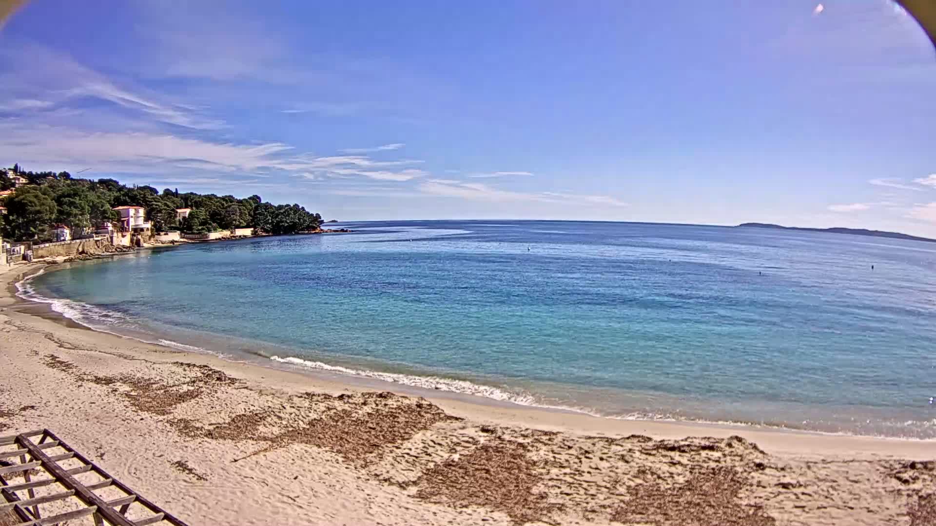 A sandy beach curves gently into a calm, turquoise sea under a clear blue sky.