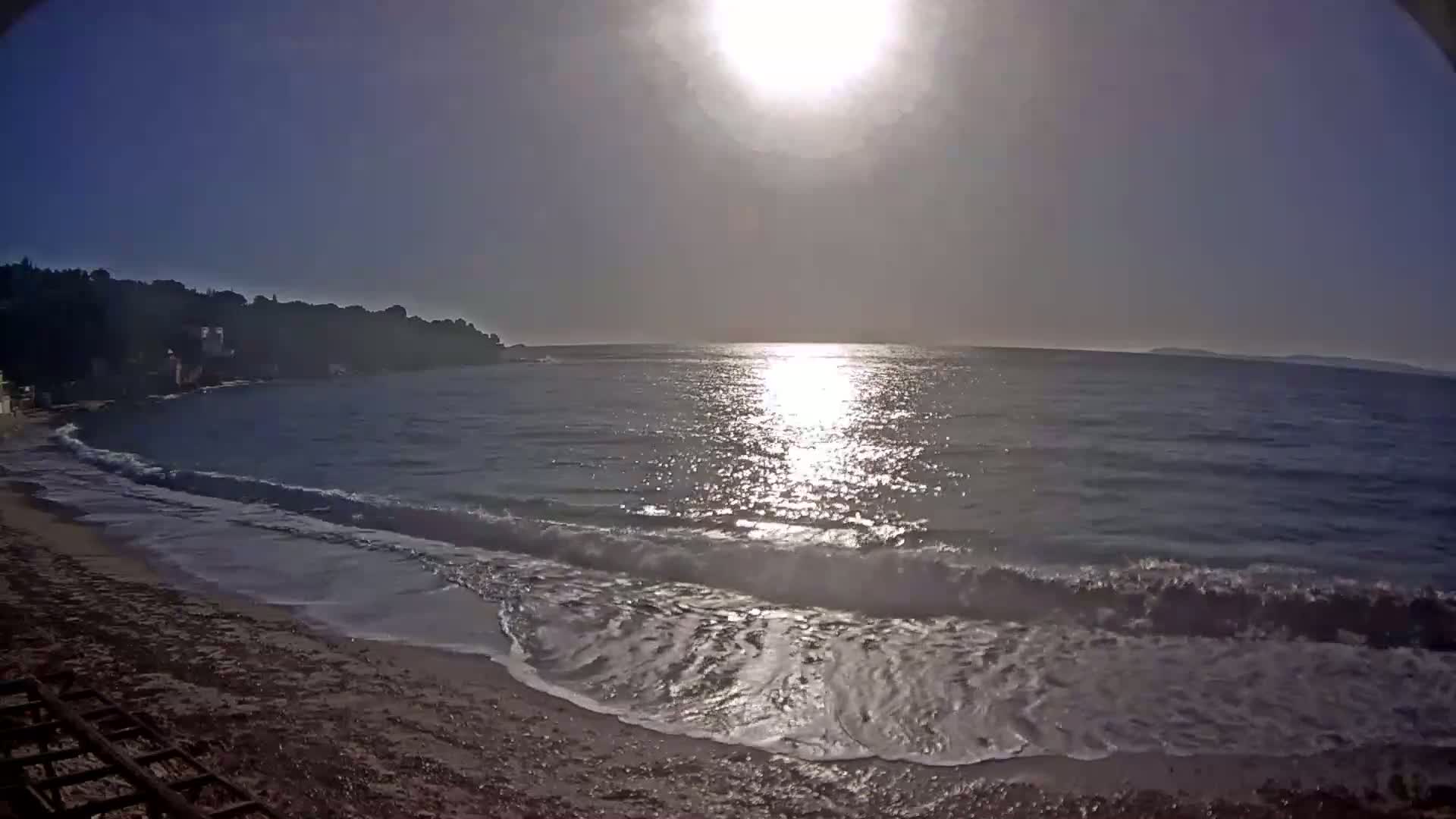 A sandy beach meets a calm sea under a bright sun.