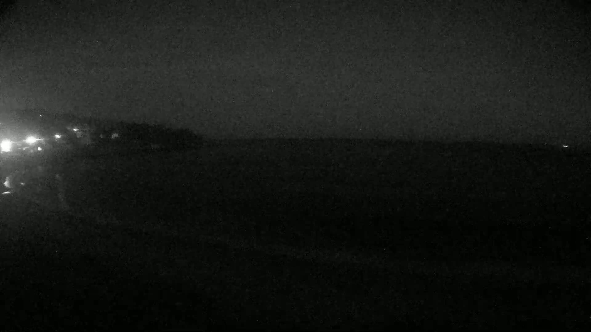 A dark, nighttime scene shows a flat, dark horizon with faint lights in the distance.
