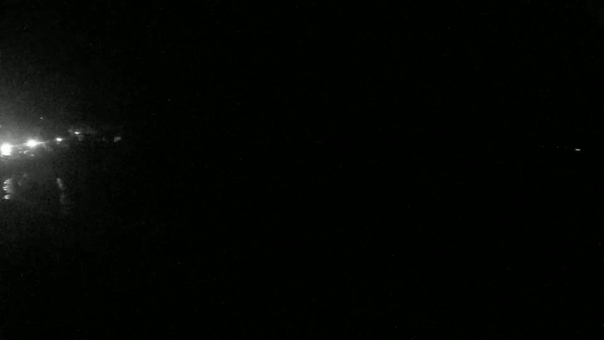 A nighttime image shows bright lights in the distance to the left, with a mostly dark and grainy sky.
