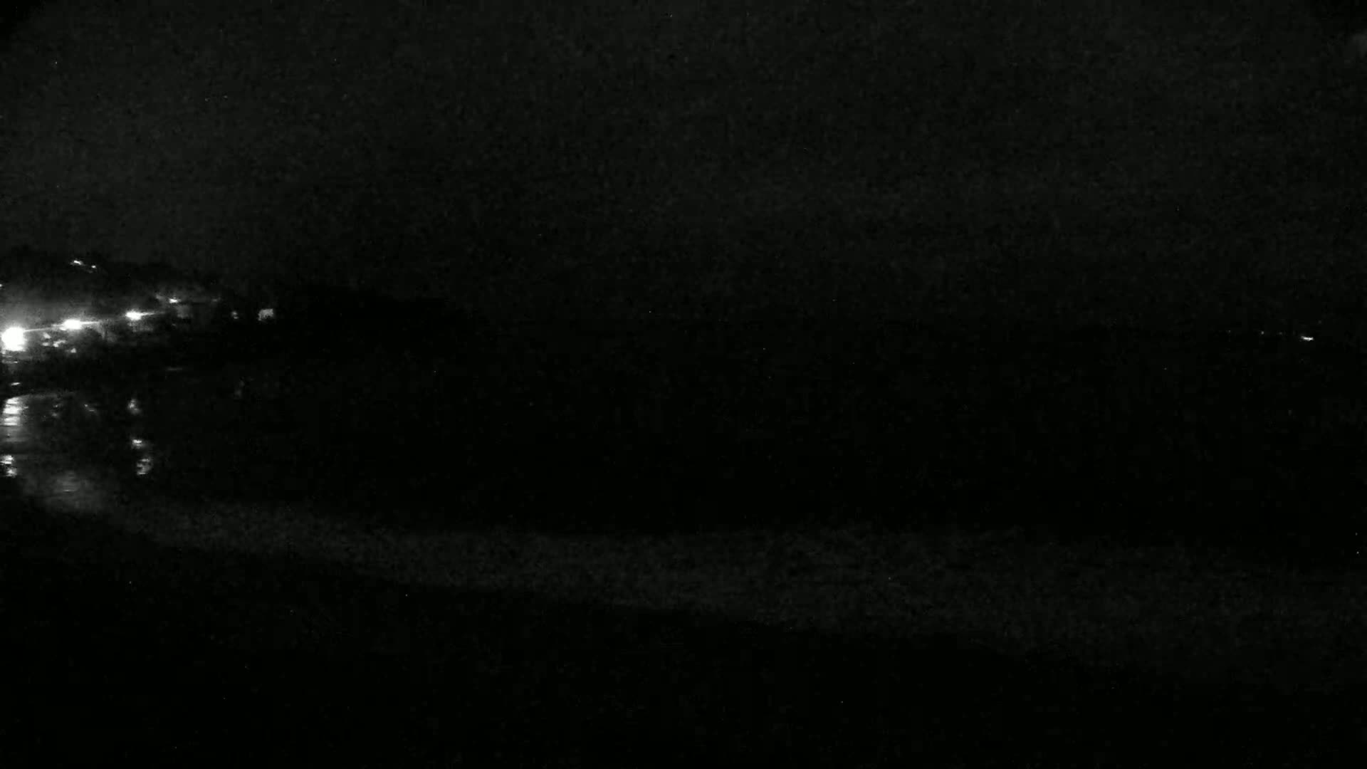 A dark, nighttime scene shows a shoreline with faint lights in the distance and a dark body of water.