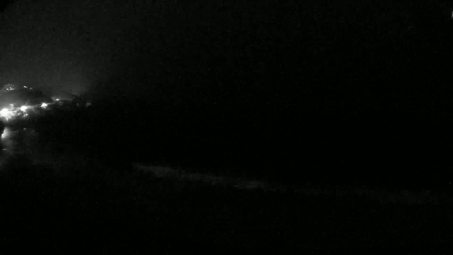 A nighttime, low-light image shows a dark sky with bright flashes of lightning in a distant, dark cloud formation.
