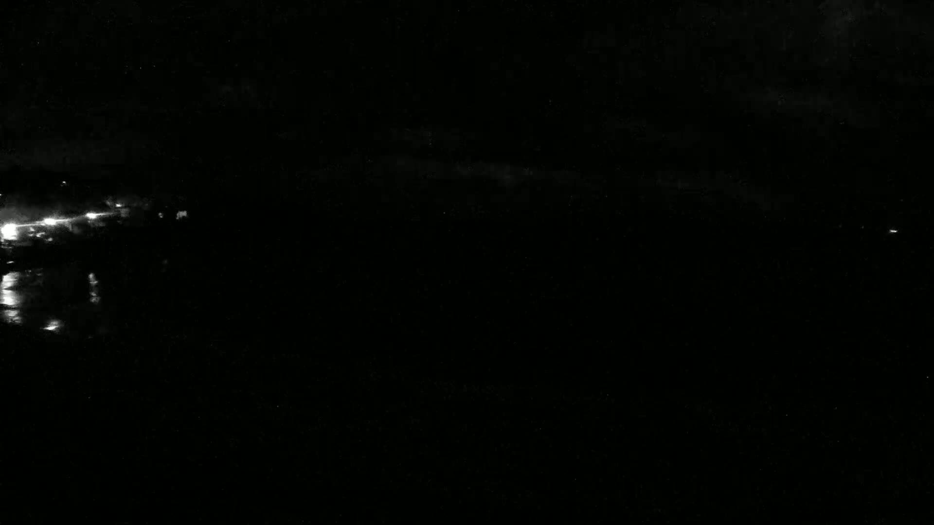 A dark nighttime scene shows a body of water reflecting a few distant lights under a mostly clear sky.
