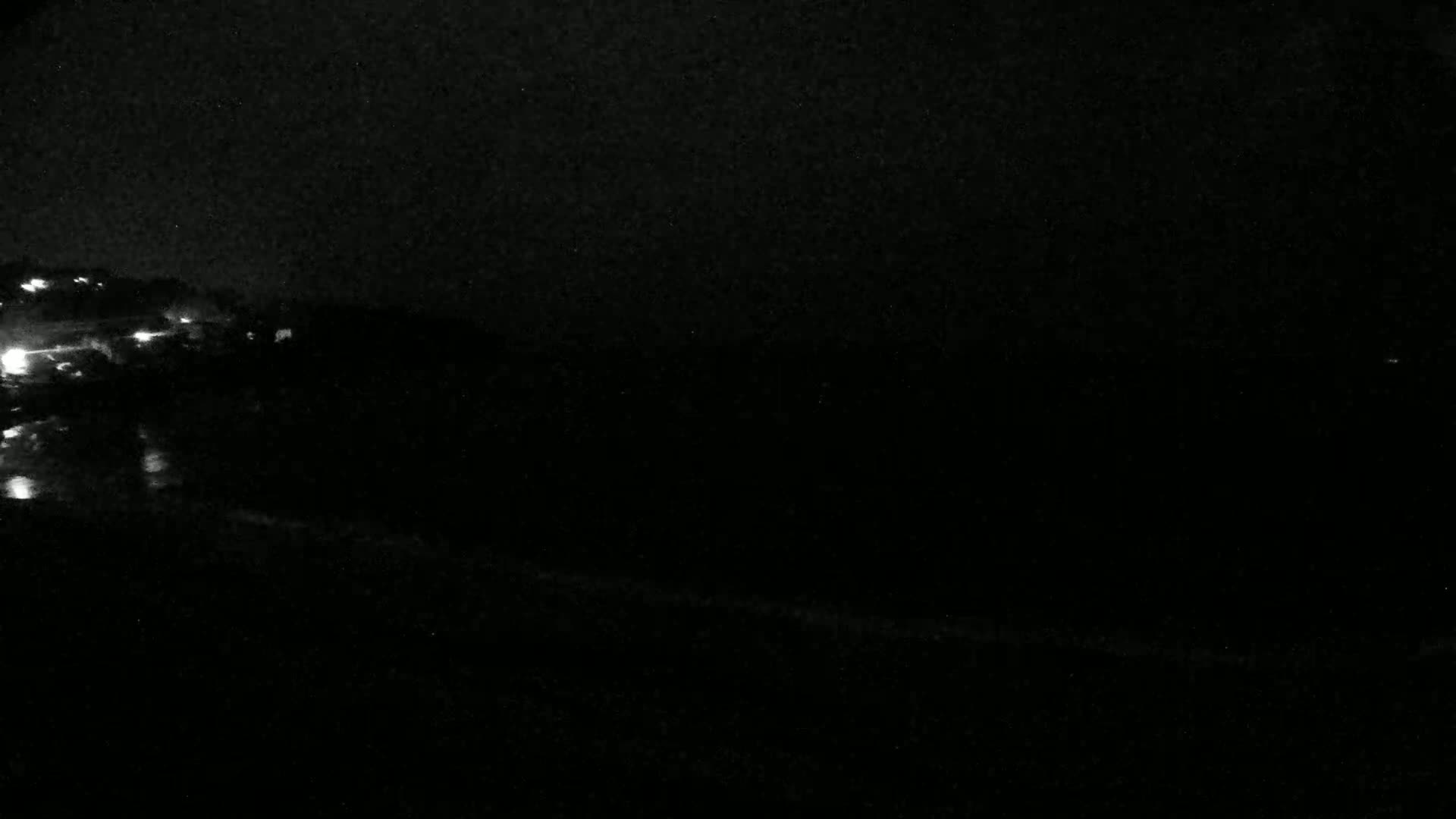A dark, nighttime scene shows a body of water with faint lights on the far left and a dark shoreline.