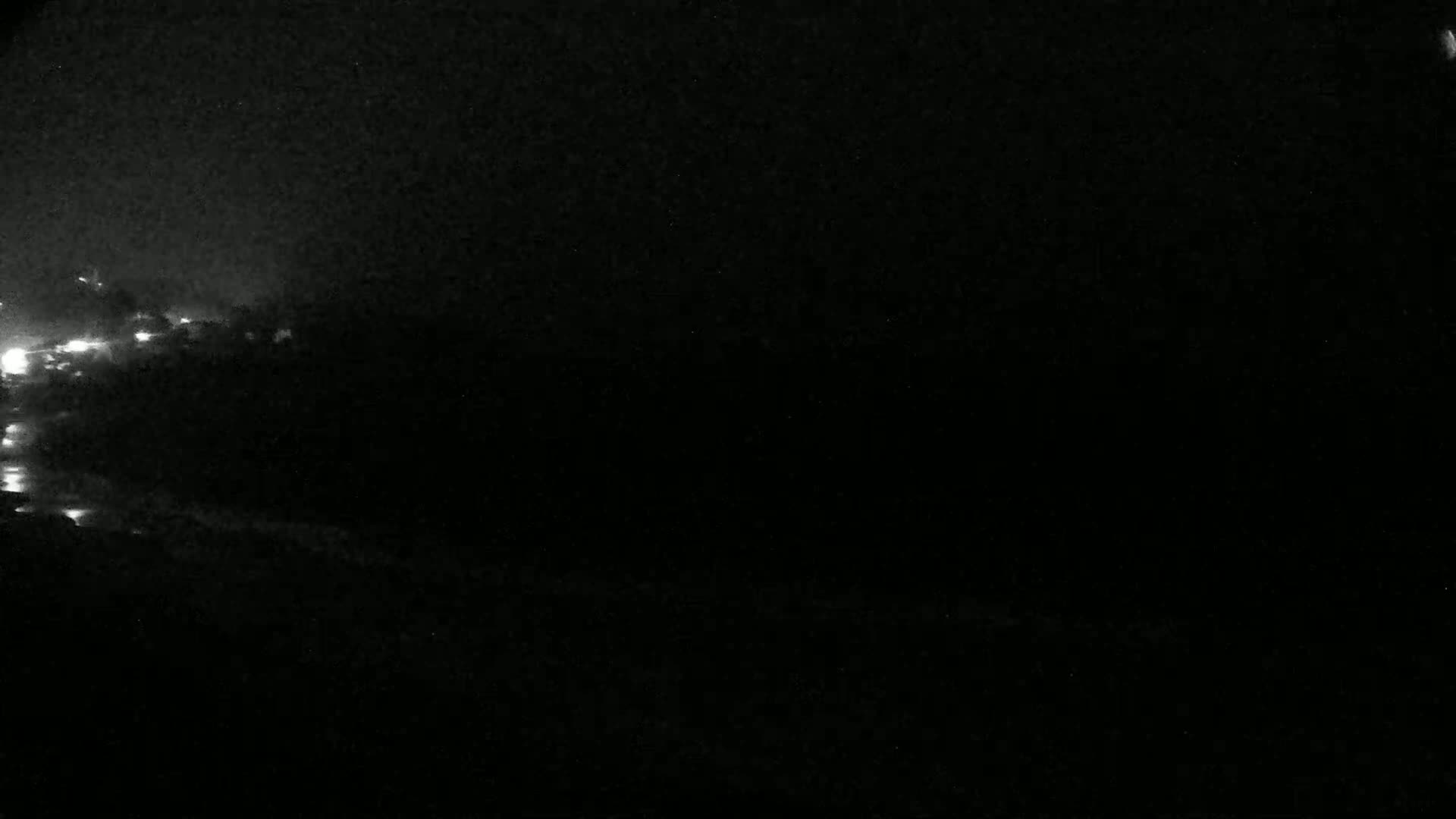 A nighttime image shows a dark landscape with a few faint lights in the distance under a dark, possibly cloudy sky.