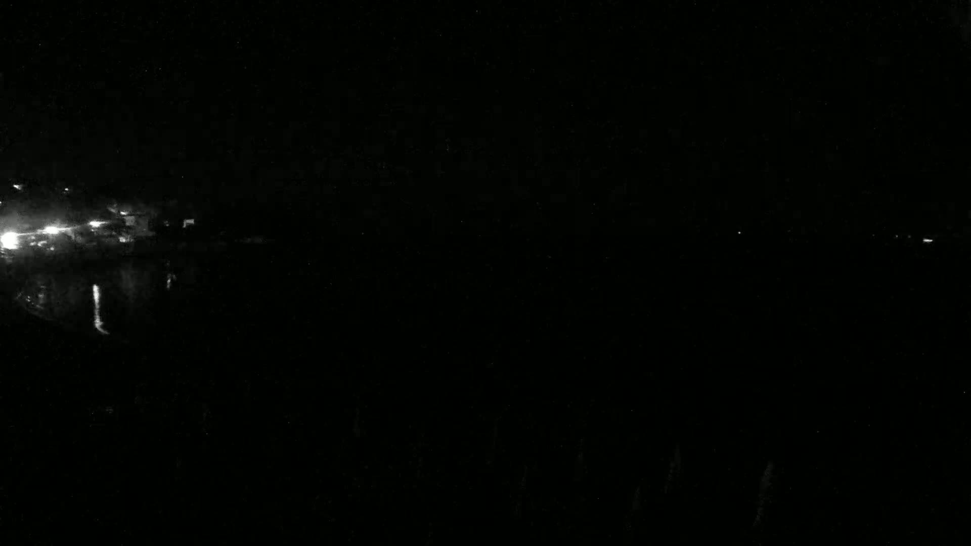 A dark nighttime scene shows a few faint lights in the distance across a body of water.