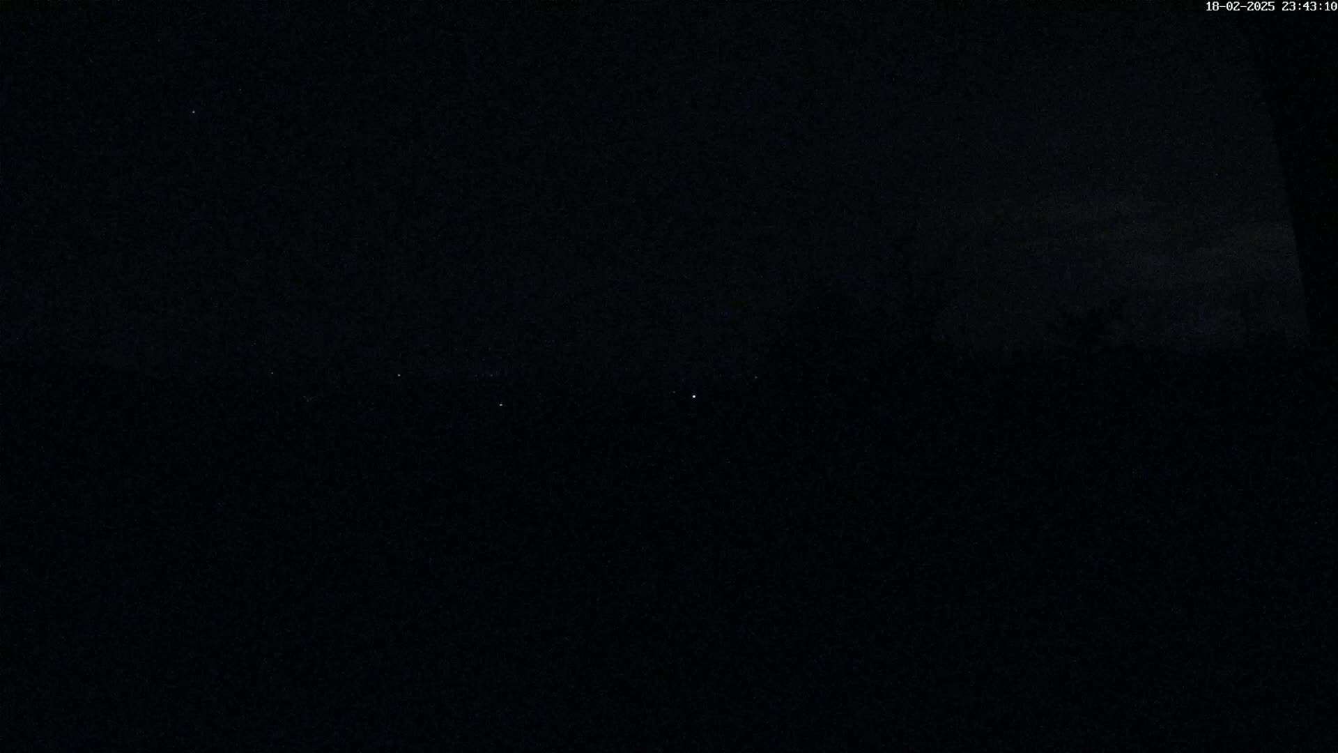 A dark, nighttime scene shows a few faint lights on the horizon under a mostly clear sky.