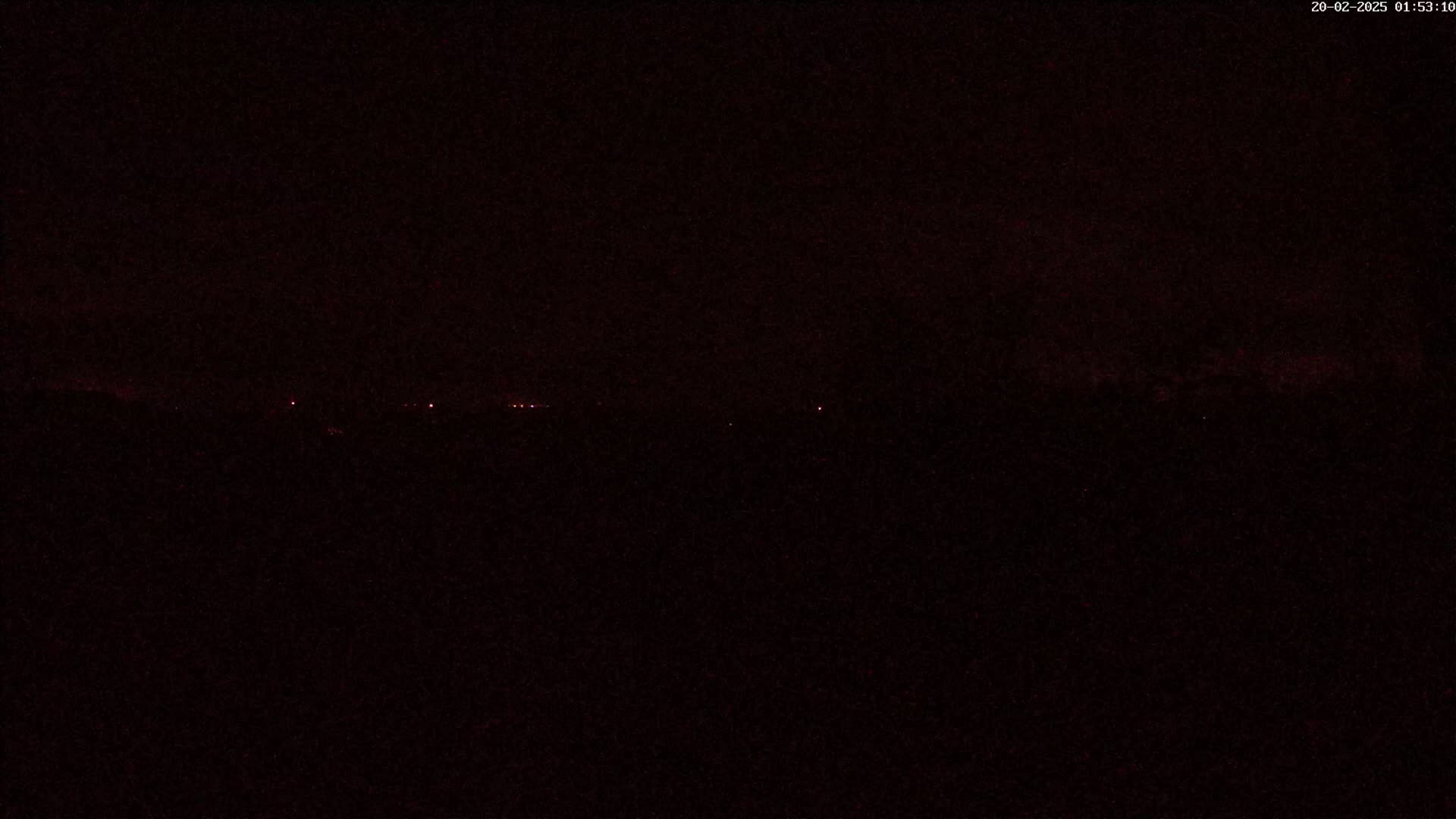 A dark, nighttime landscape shows a faint, distant line of red lights on the horizon.