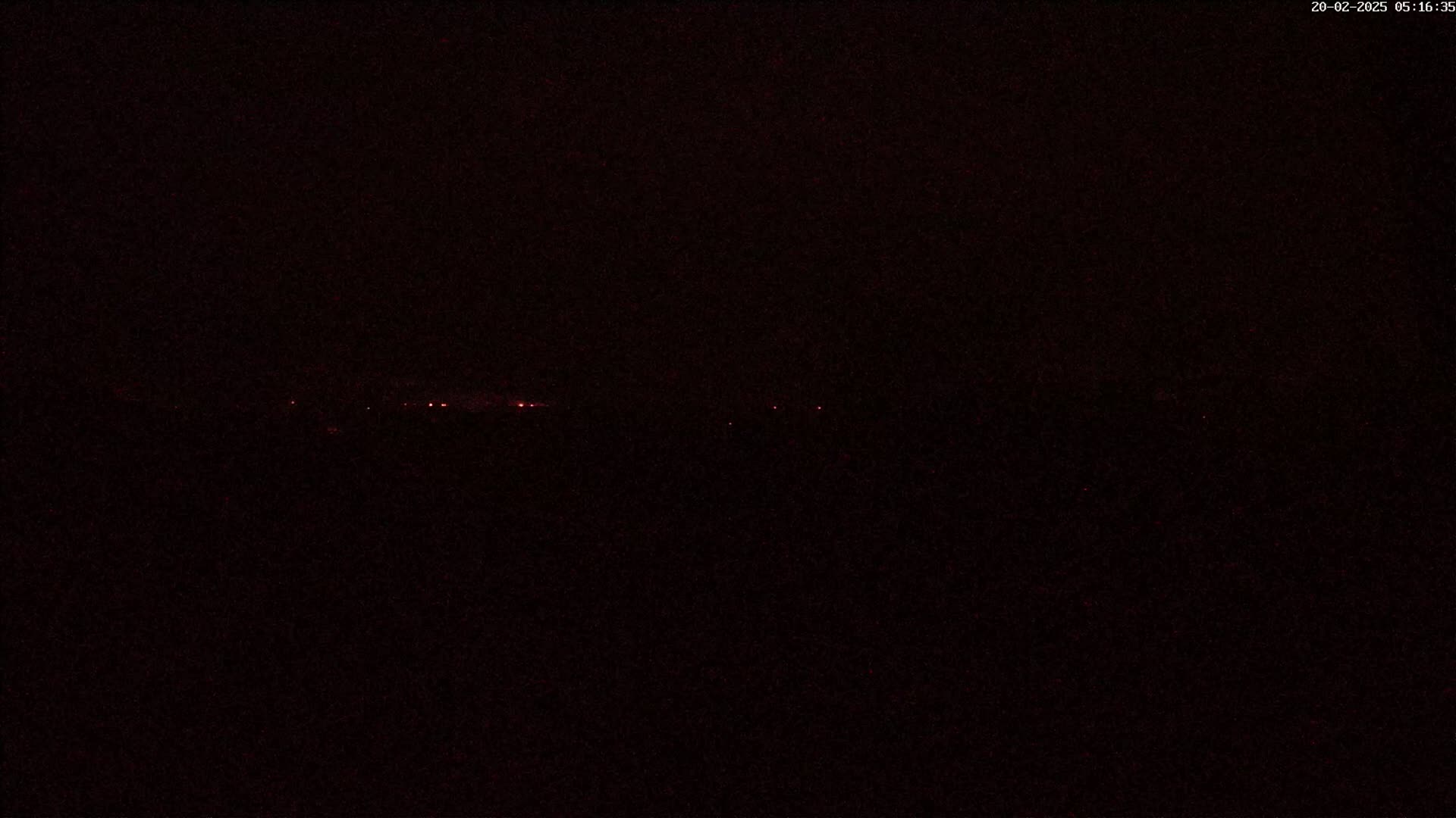A dark nighttime scene shows a faint, distant line of red lights on the horizon.