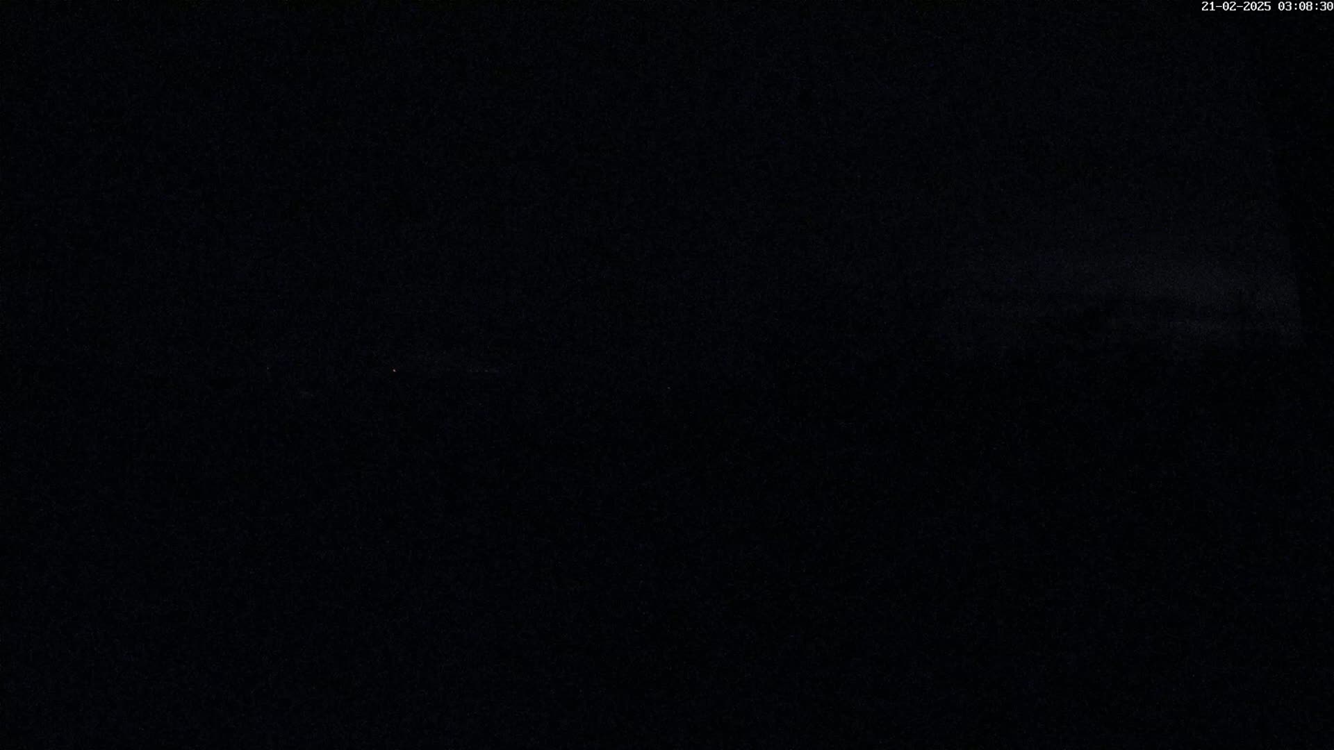 A dark, nighttime scene shows a mostly black expanse with a hint of very faint light in the distance.
