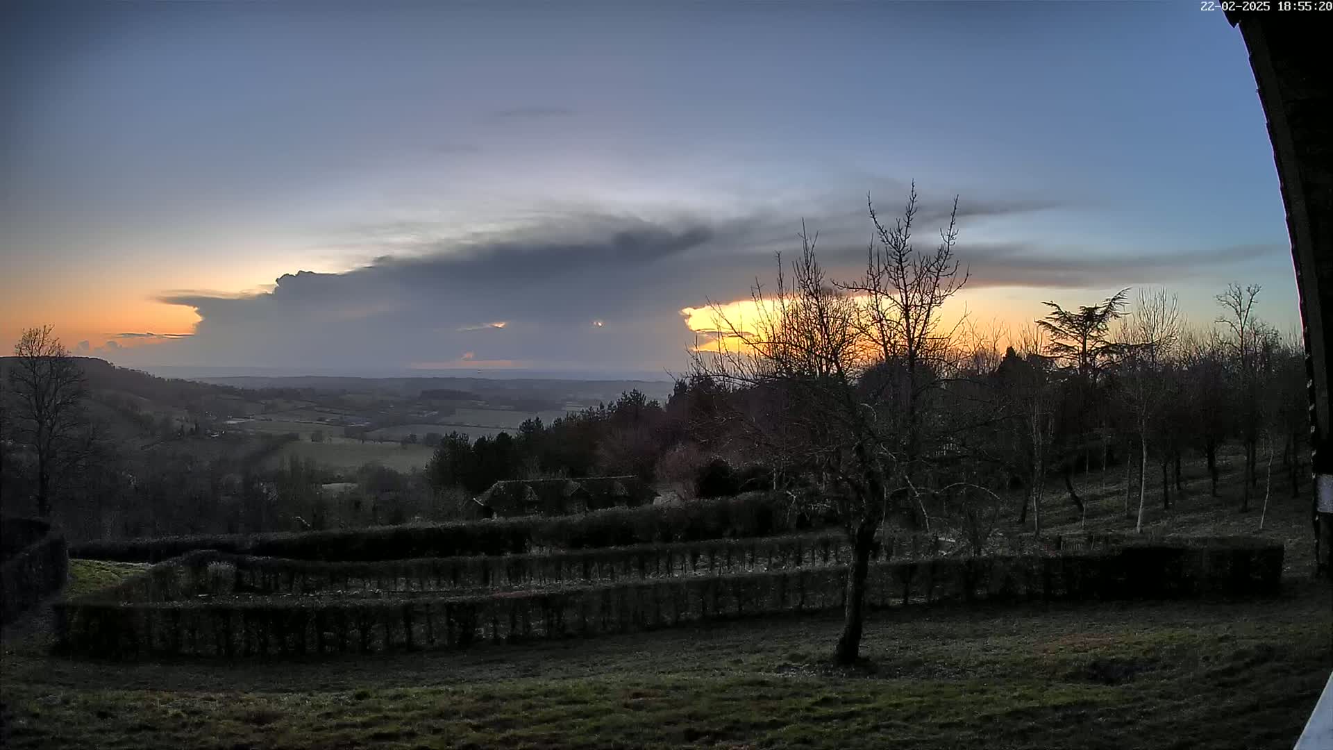 A sunset over a rural landscape with dark, ominous clouds in the sky, viewed from a slightly elevated position showing a field with hedges.