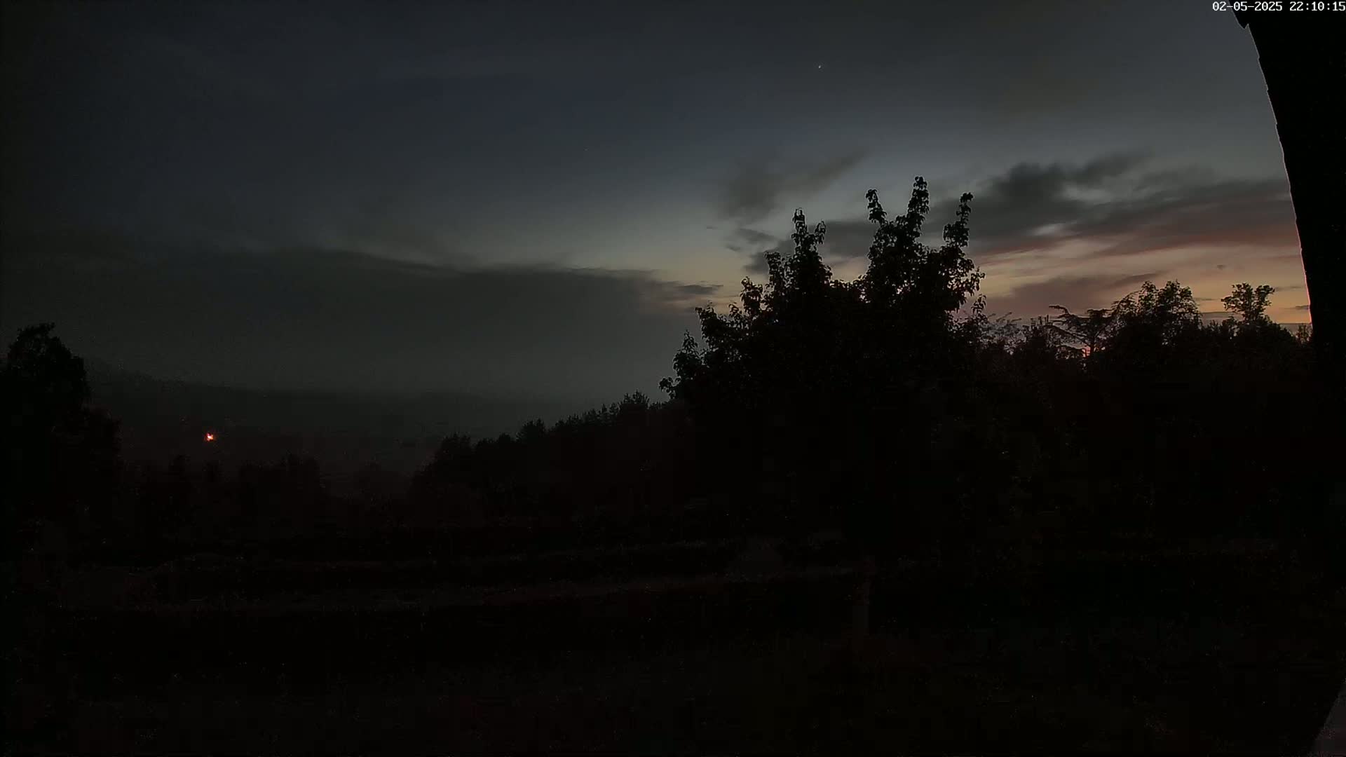 Silhouetted trees and a distant, hazy landscape are visible under a partly cloudy, twilight sky.