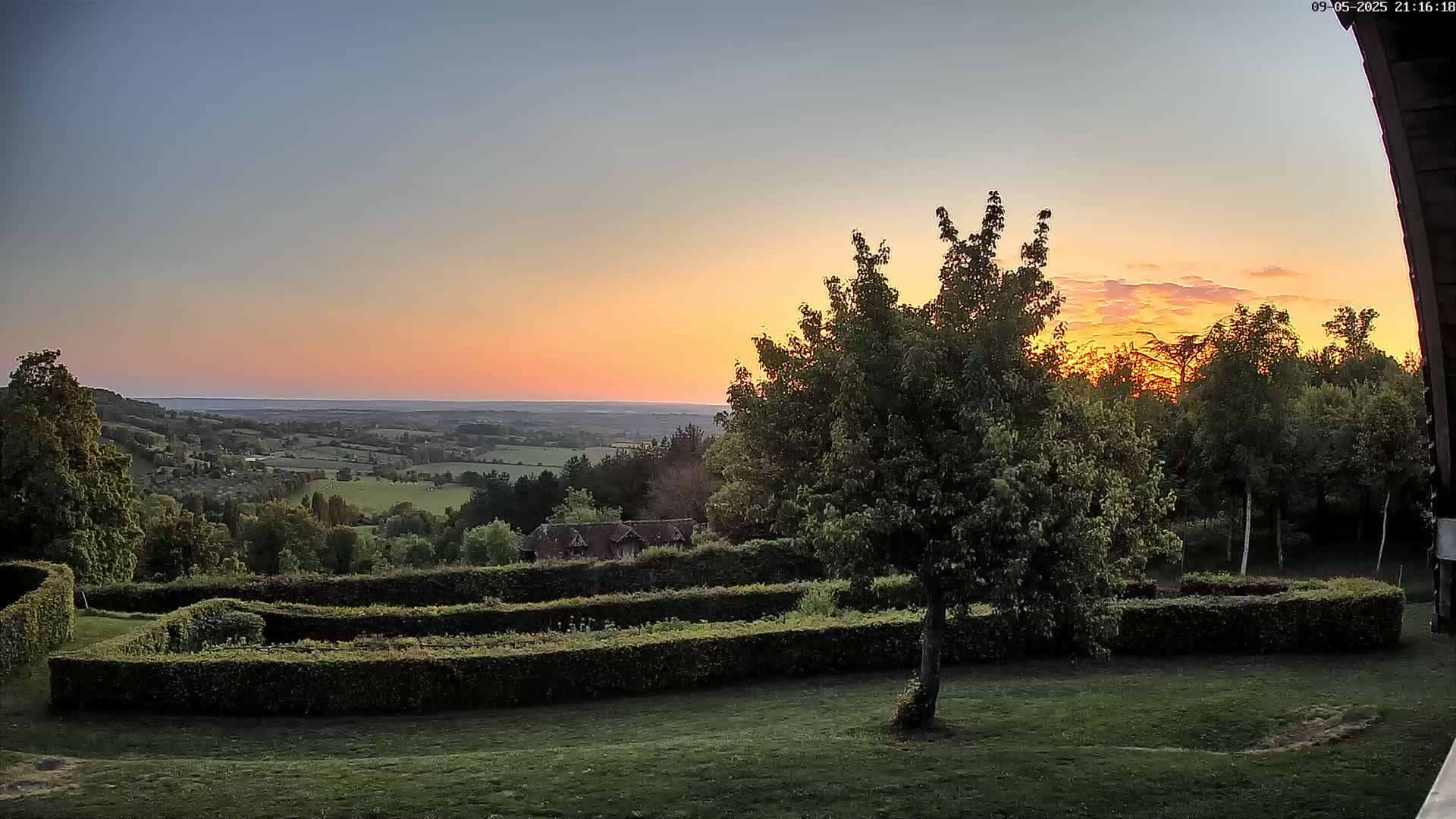A sunset over a hilly landscape with a neatly trimmed hedge garden in the foreground.