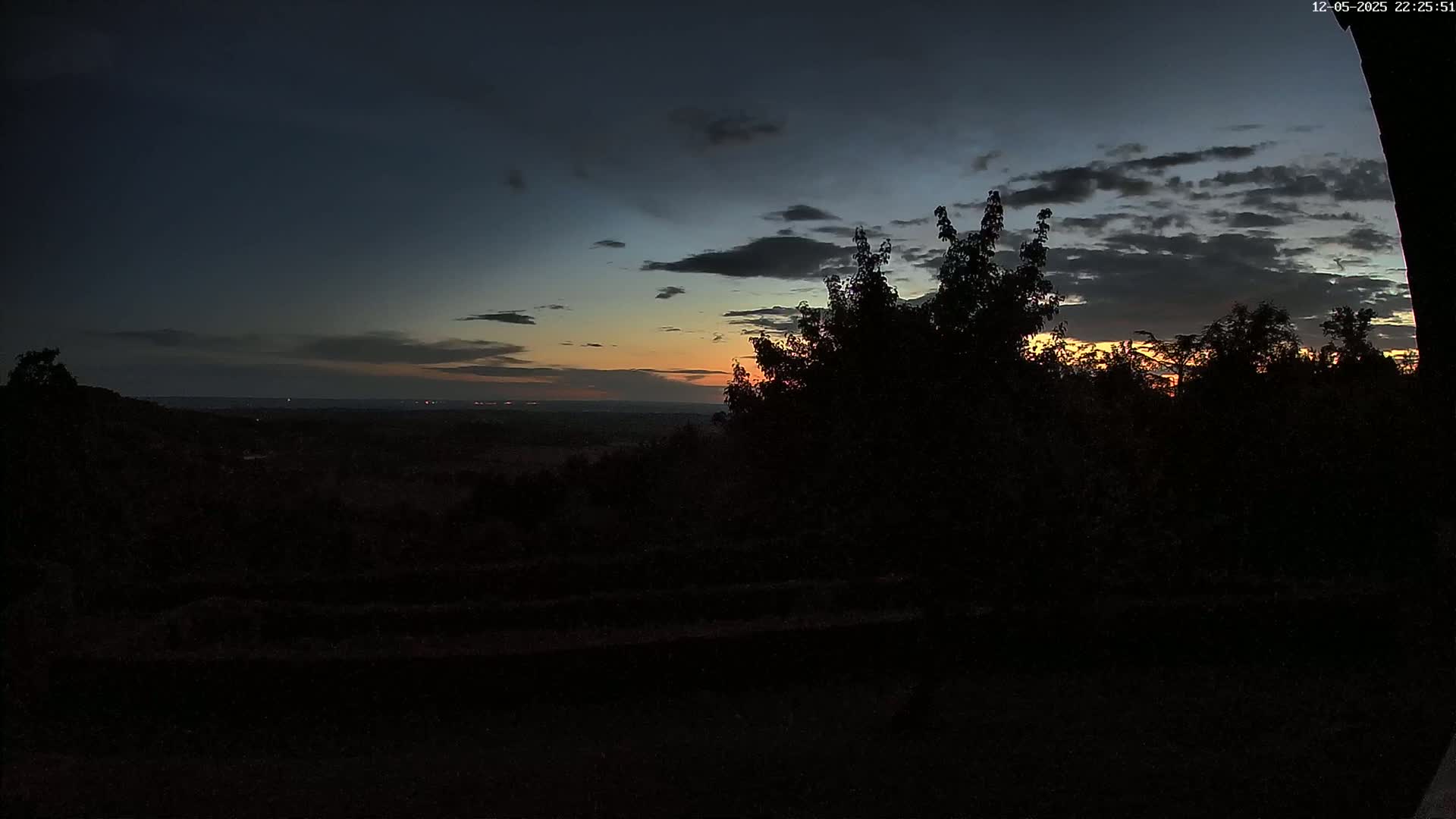 Silhouetted trees and a distant landscape are visible at twilight under a partly cloudy sky.