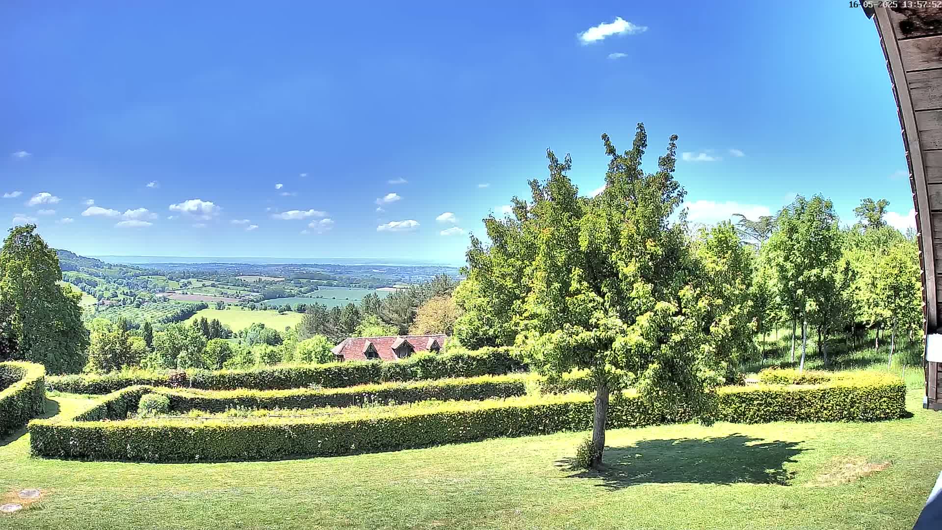A lush green lawn with a sculpted hedge garden overlooks a rolling countryside under a mostly sunny sky.