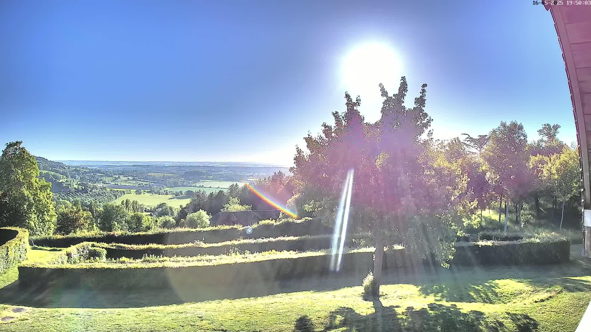 A sunny day reveals a sprawling green landscape with rolling hills and neatly trimmed hedges, viewed from a slightly elevated position.