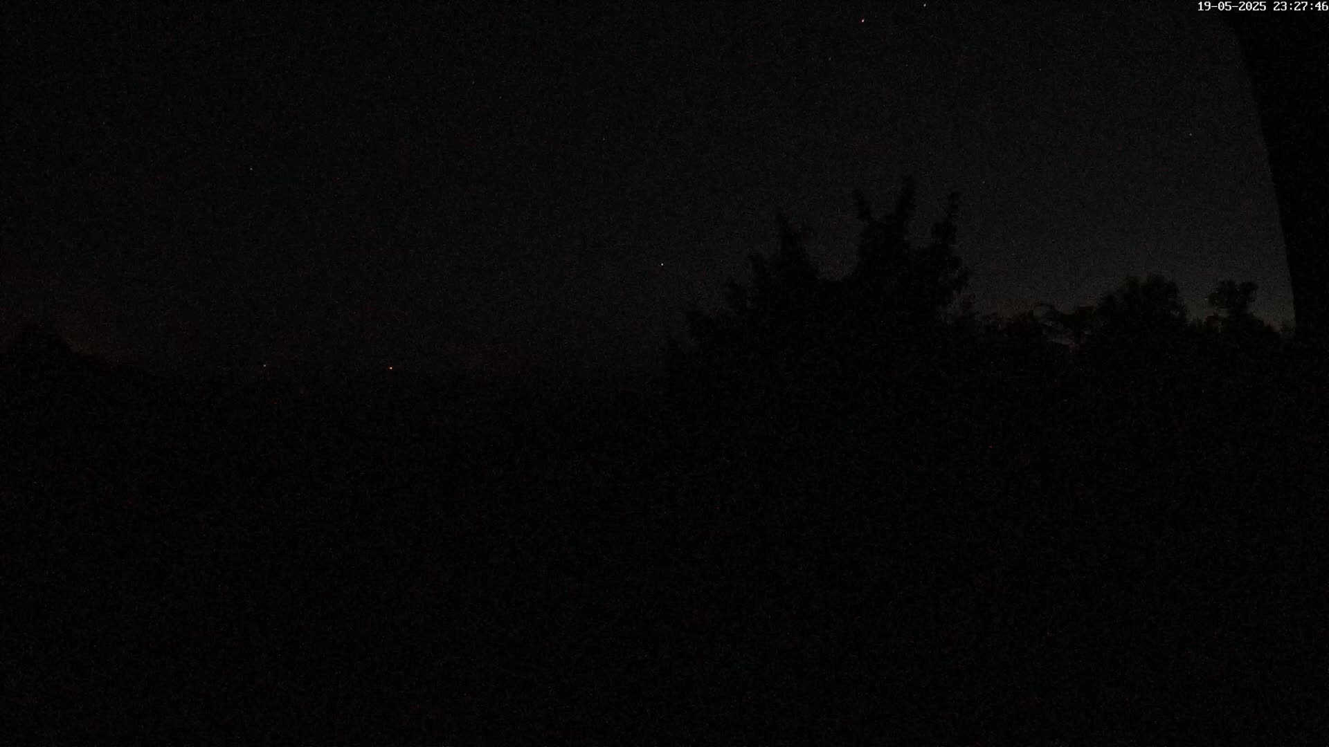 A nighttime, dark scene shows a few stars in the sky and the silhouettes of trees and possibly mountains in the distance.