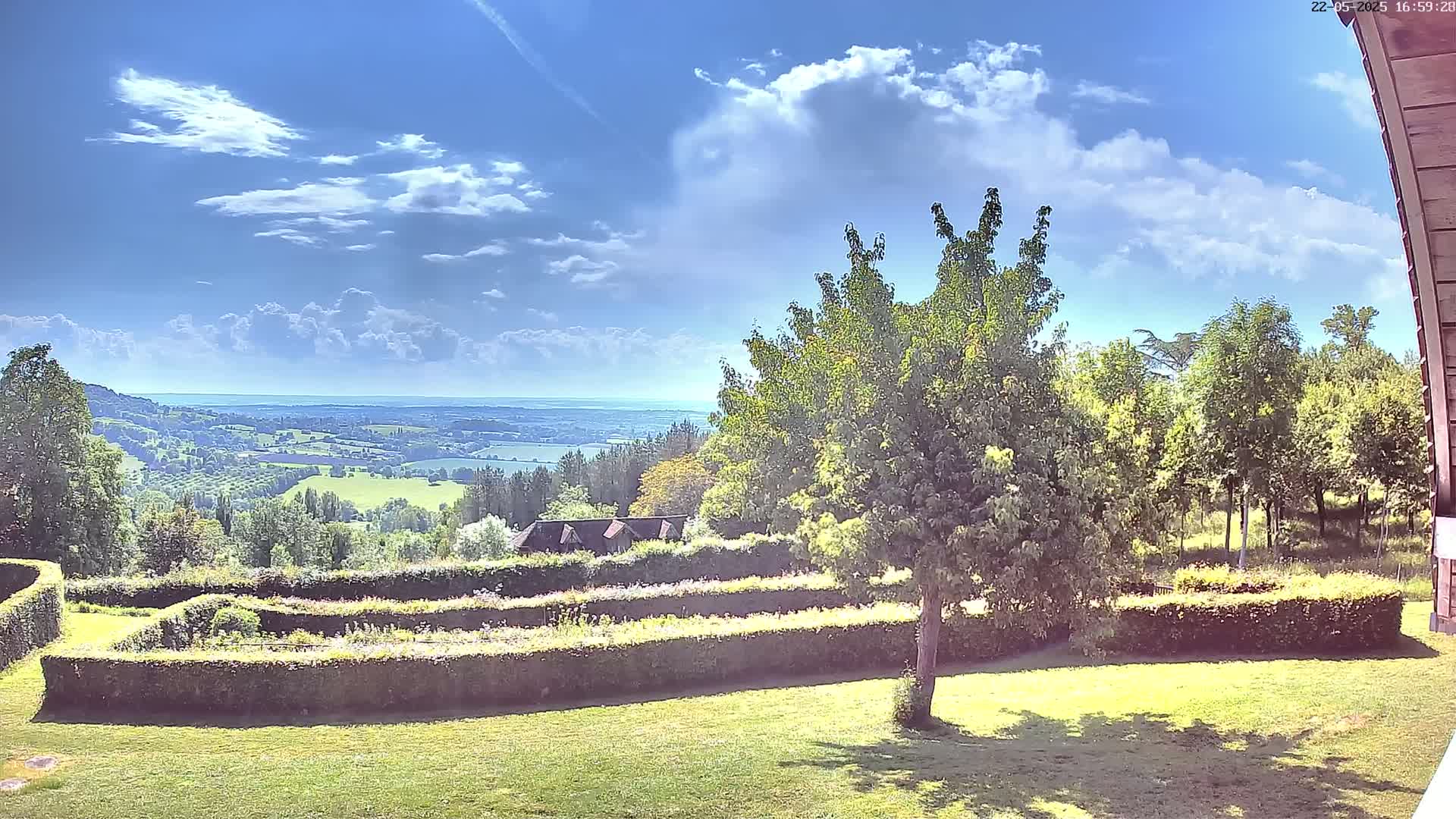 A sunny day reveals a sprawling landscape of green fields and trees, a distant body of water, and a manicured garden with hedges.