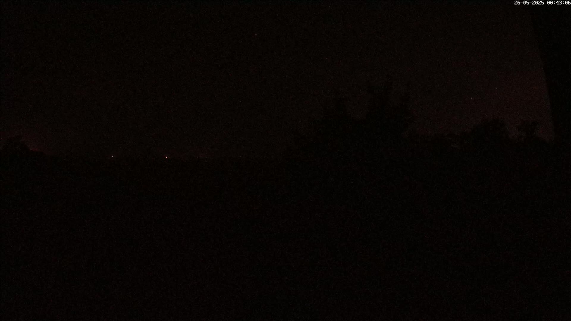 A dark nighttime scene shows a mostly obscured landscape with a few faint lights on the horizon under a mostly clear, starlit sky.