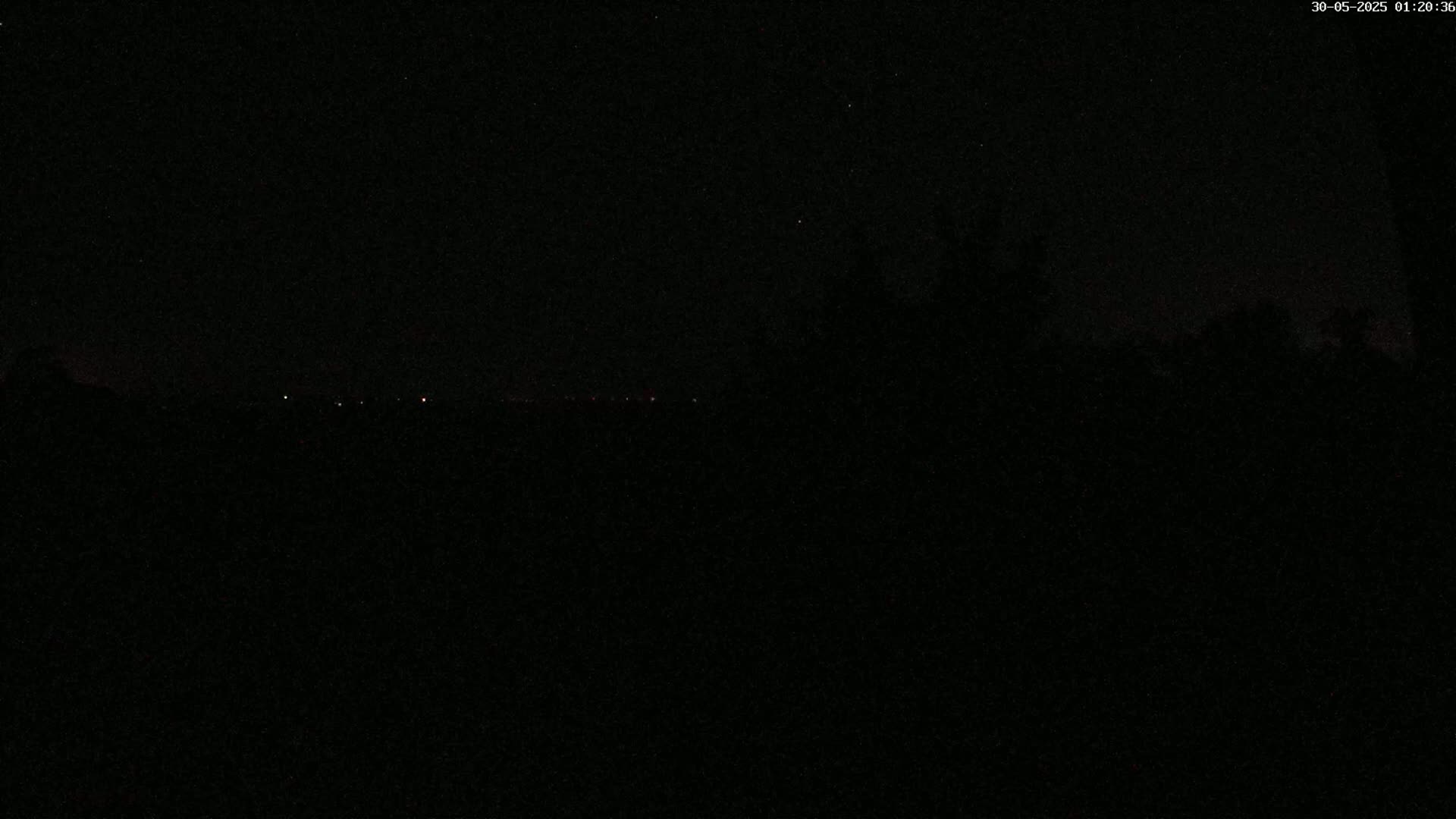 A nighttime scene shows a dark landscape with a few distant lights visible on the horizon under a mostly clear, dark sky.