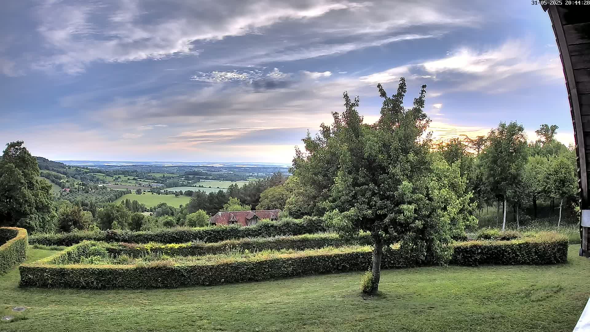 A sprawling green landscape with a neatly trimmed hedge and a distant view of a calm body of water under a partly cloudy sky.