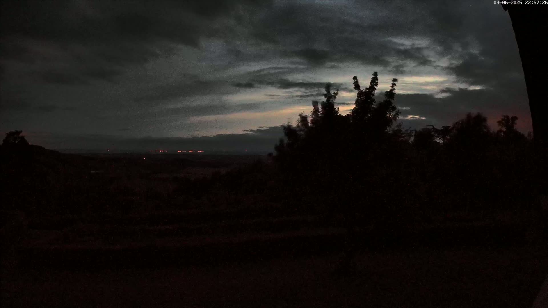 A dark, overcast sky with hints of twilight shows over a silhouetted landscape of trees and distant lights.