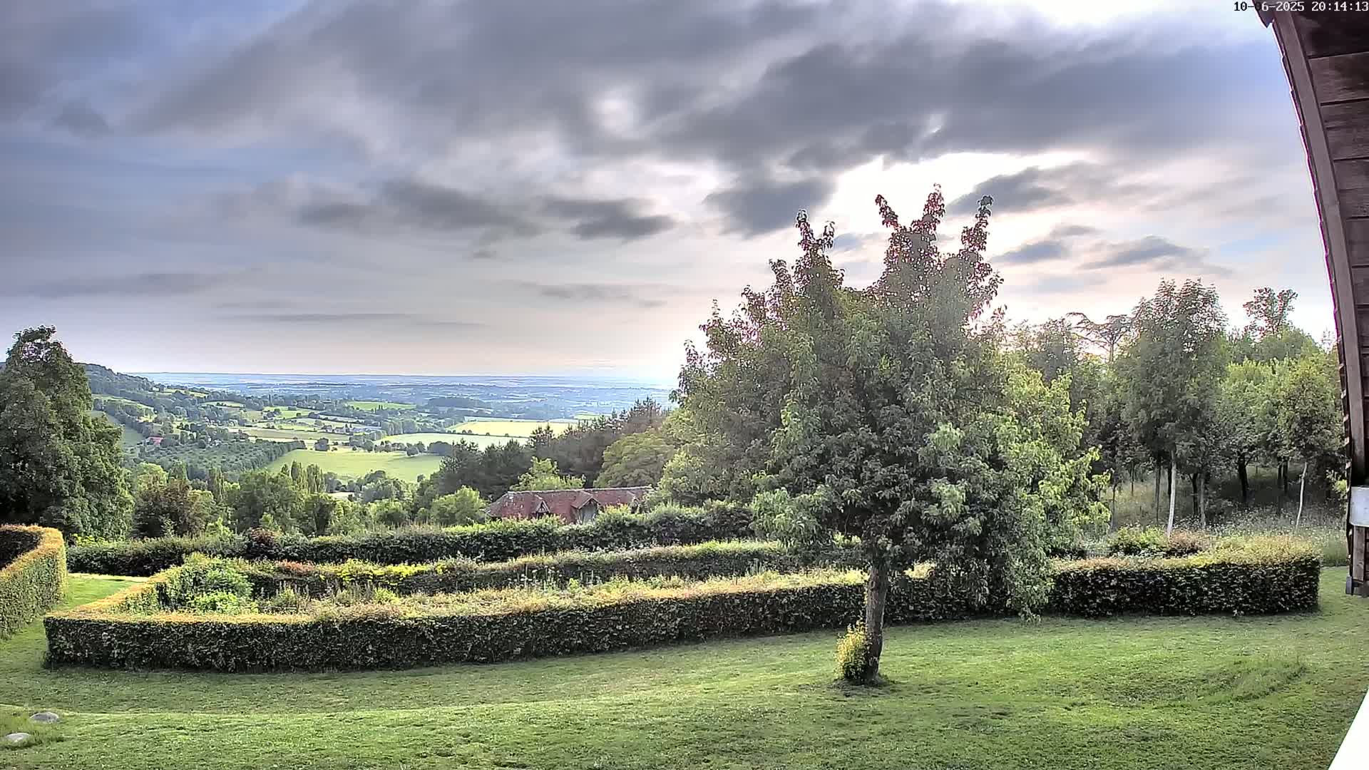 A verdant garden with neatly trimmed hedges overlooks a sprawling countryside under a cloudy sky.