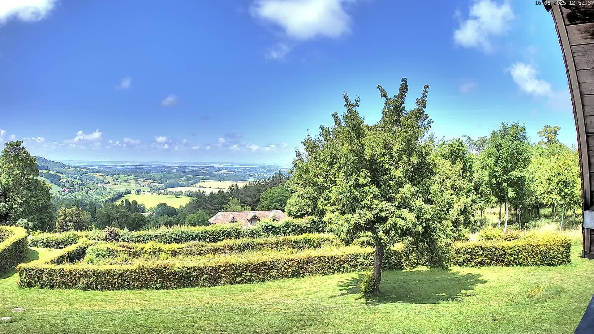 A verdant garden with neatly trimmed hedges overlooks a sprawling countryside under a mostly sunny sky.