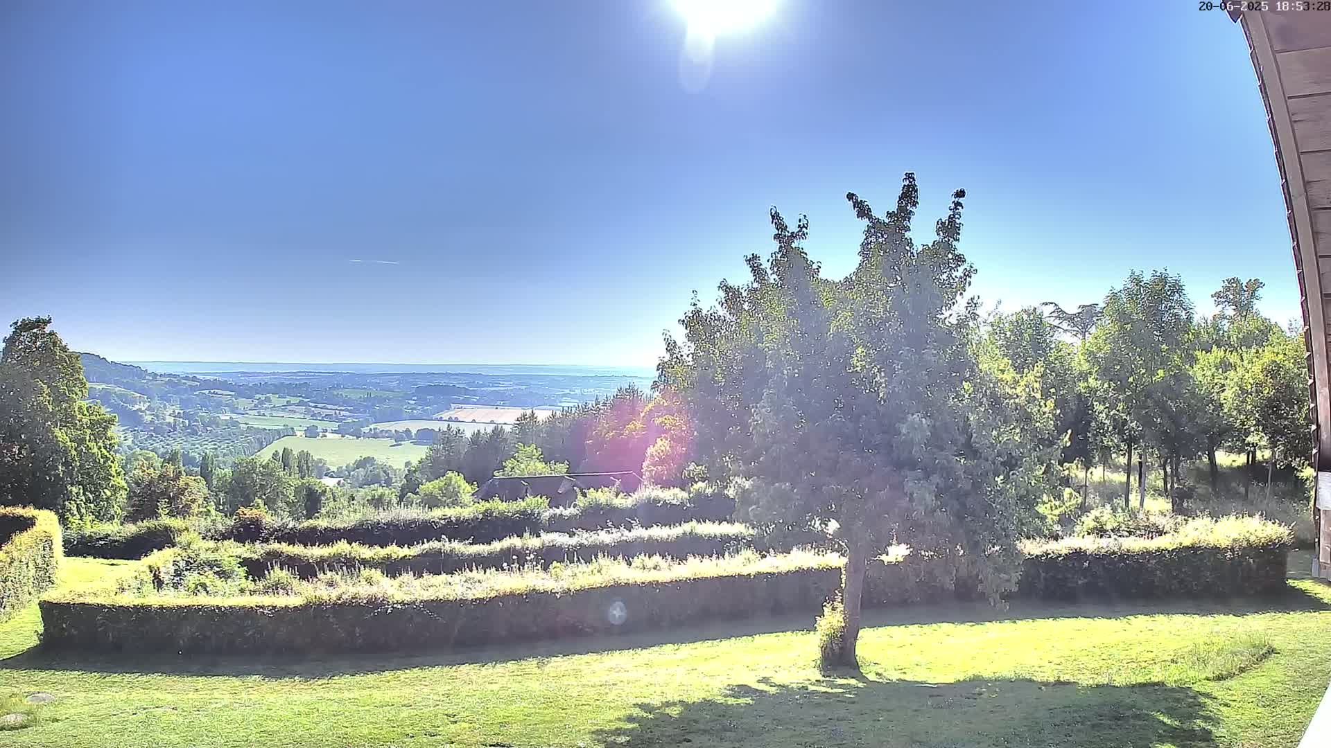 A sunny day reveals a verdant landscape with neatly trimmed hedges, a sprawling tree, and a distant valley extending to a hazy horizon.