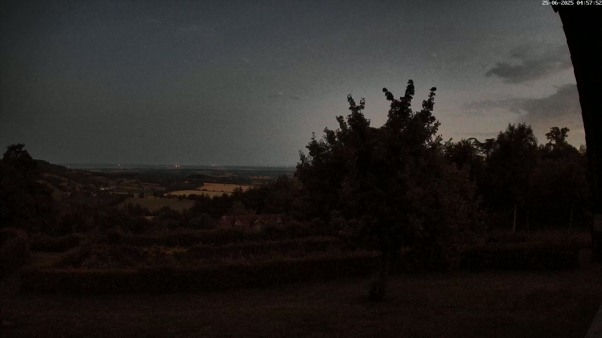 A dark, overcast sky hangs over a landscape of rolling hills and trees at twilight.
