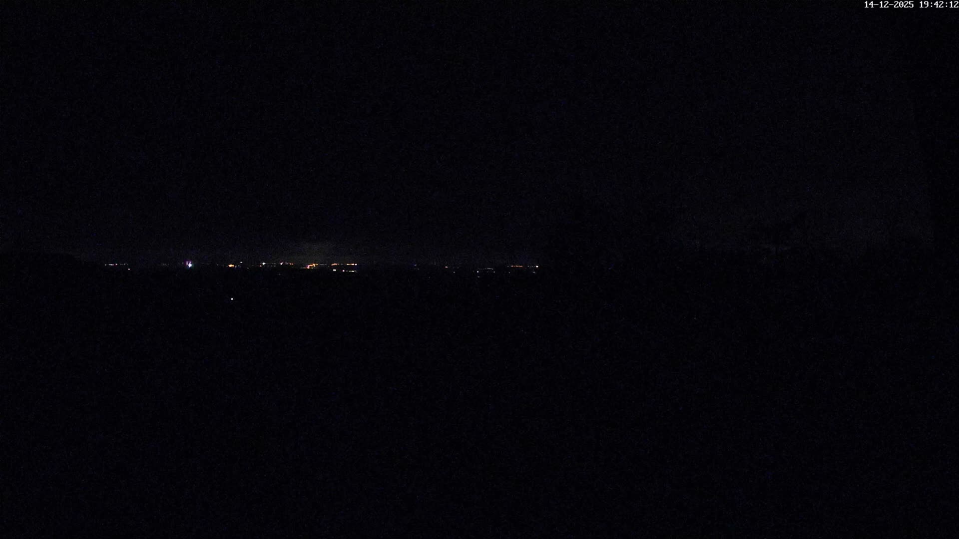 Under an overcast and misty sky, a green lawn and a dark hedgerow garden lead the eye to a partially obscured house nestled among rolling green and wooded hills stretching to the horizon.