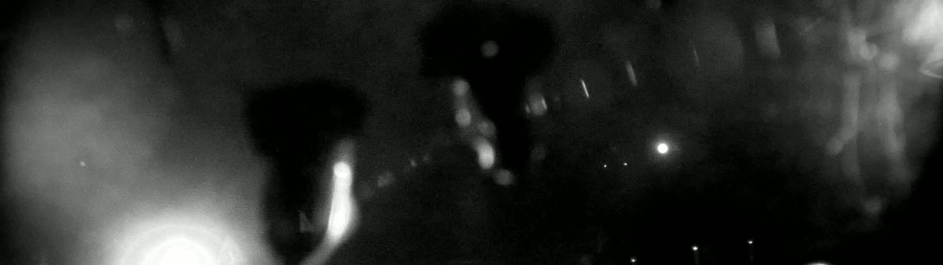 Blurry, out-of-focus shapes and lights are visible in the dark, possibly during rain.