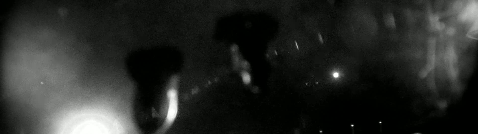 A blurry, dark image shows indistinct shapes and a few bright lights in the distance under a rainy night sky.