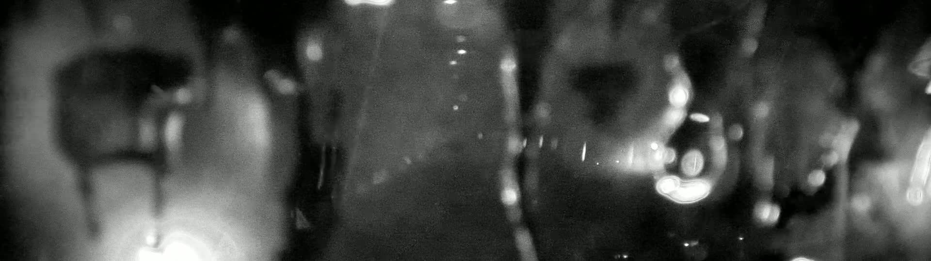 Blurry, out-of-focus shapes and lights are visible through a rain-streaked surface at night.