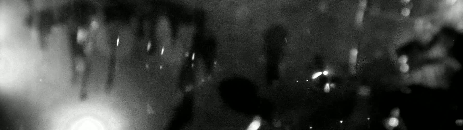 Blurred, out-of-focus nighttime imagery shows indistinct shapes and bright lights through what appears to be rain or moisture on a surface.