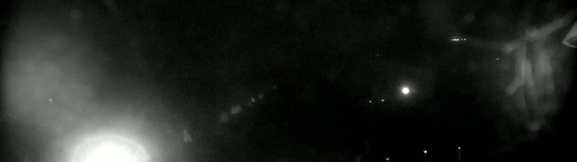 A hazy, dark nighttime scene shows several faint lights in the distance, with brighter lights closer to the bottom of the frame.