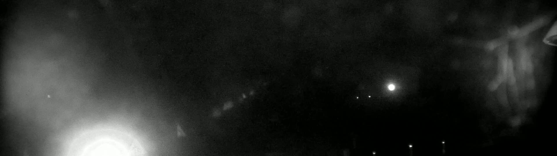 A nighttime, hazy scene shows a bright light in the lower left and several fainter lights in the distance, with a mostly dark sky.