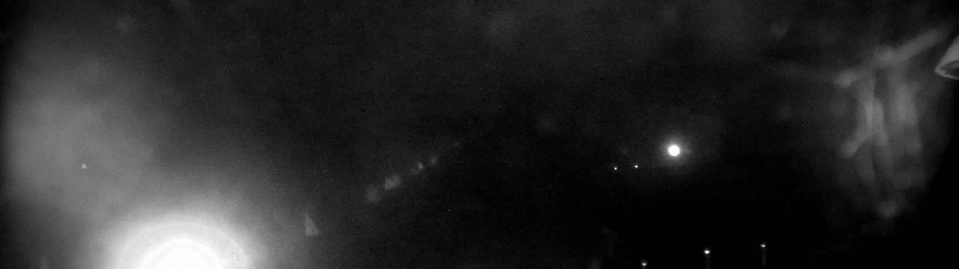 A nighttime outdoor scene shows a bright light in the lower left corner and several fainter lights in the distance, with a hazy or foggy atmosphere.