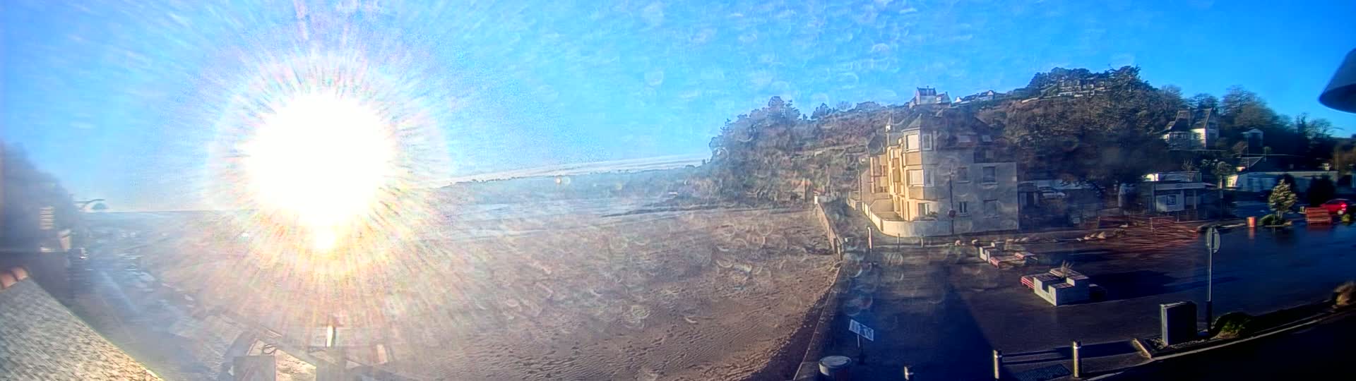 A bright, sunny day reveals a sandy beach next to a hillside of buildings and trees.