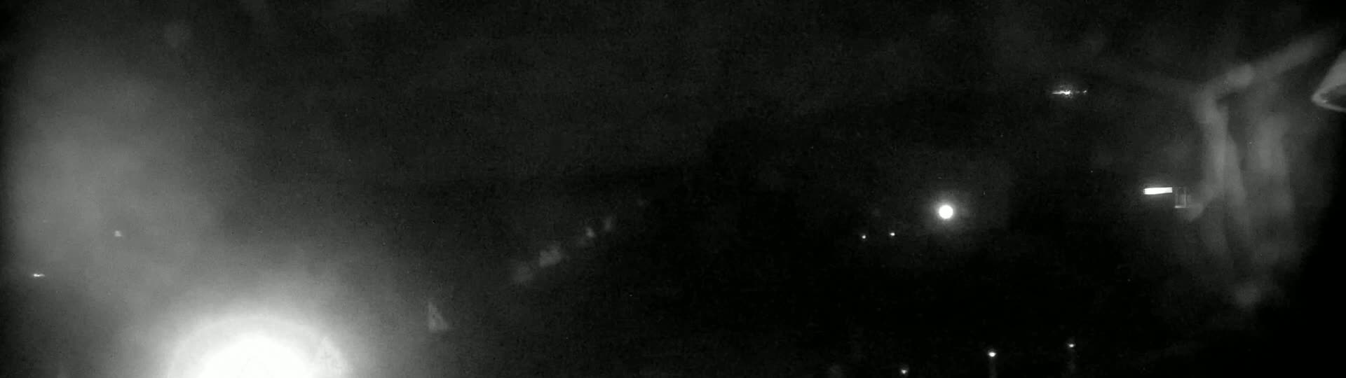 A blurry, nighttime image shows indistinct shapes and faint lights in hazy or foggy conditions.
