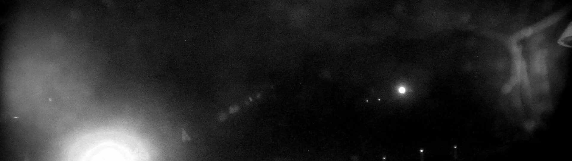 A nighttime, blurry view shows a bright light to the left and several fainter lights in the distance.