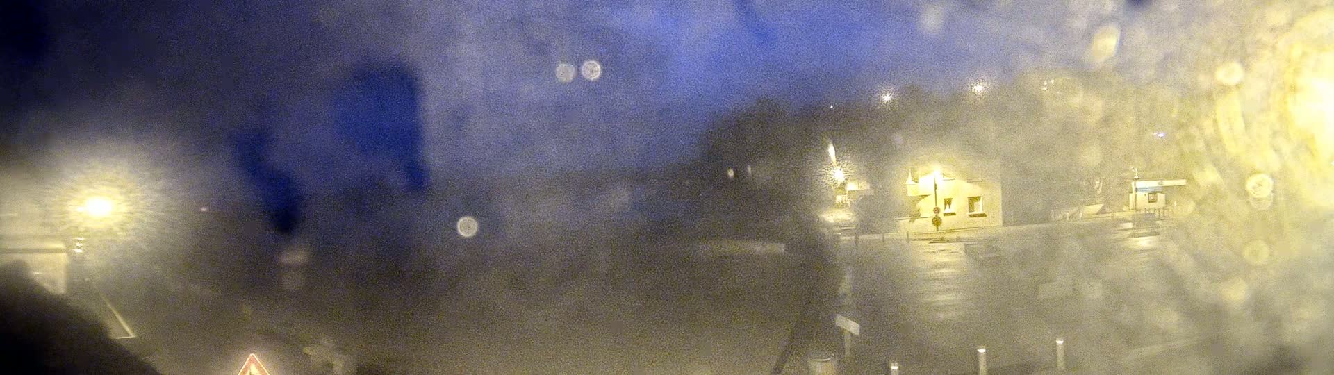 A blurry night scene viewed through a rain-streaked window shows a dimly lit street with buildings and streetlights.