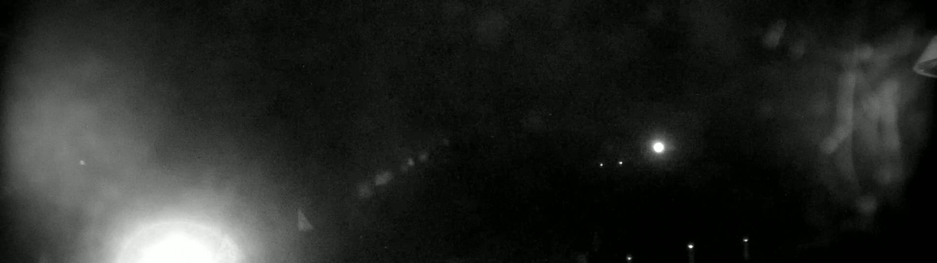 A nighttime, possibly rainy, outdoor scene shows a blurry view of lights in the distance and some brighter lights closer to the camera.
