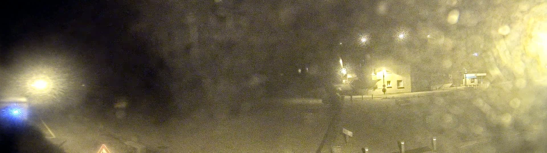 A blurry nighttime image shows a building and streetlights in snowy or foggy conditions.