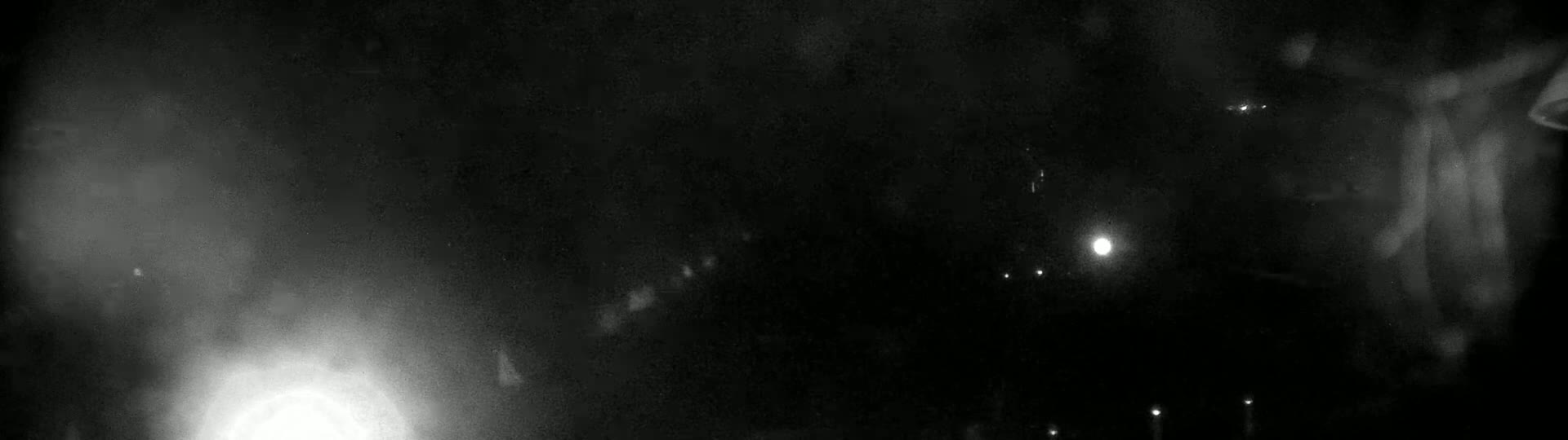 A blurry, nighttime image shows indistinct shapes and faint lights in the darkness, possibly suggesting a foggy or hazy atmosphere.